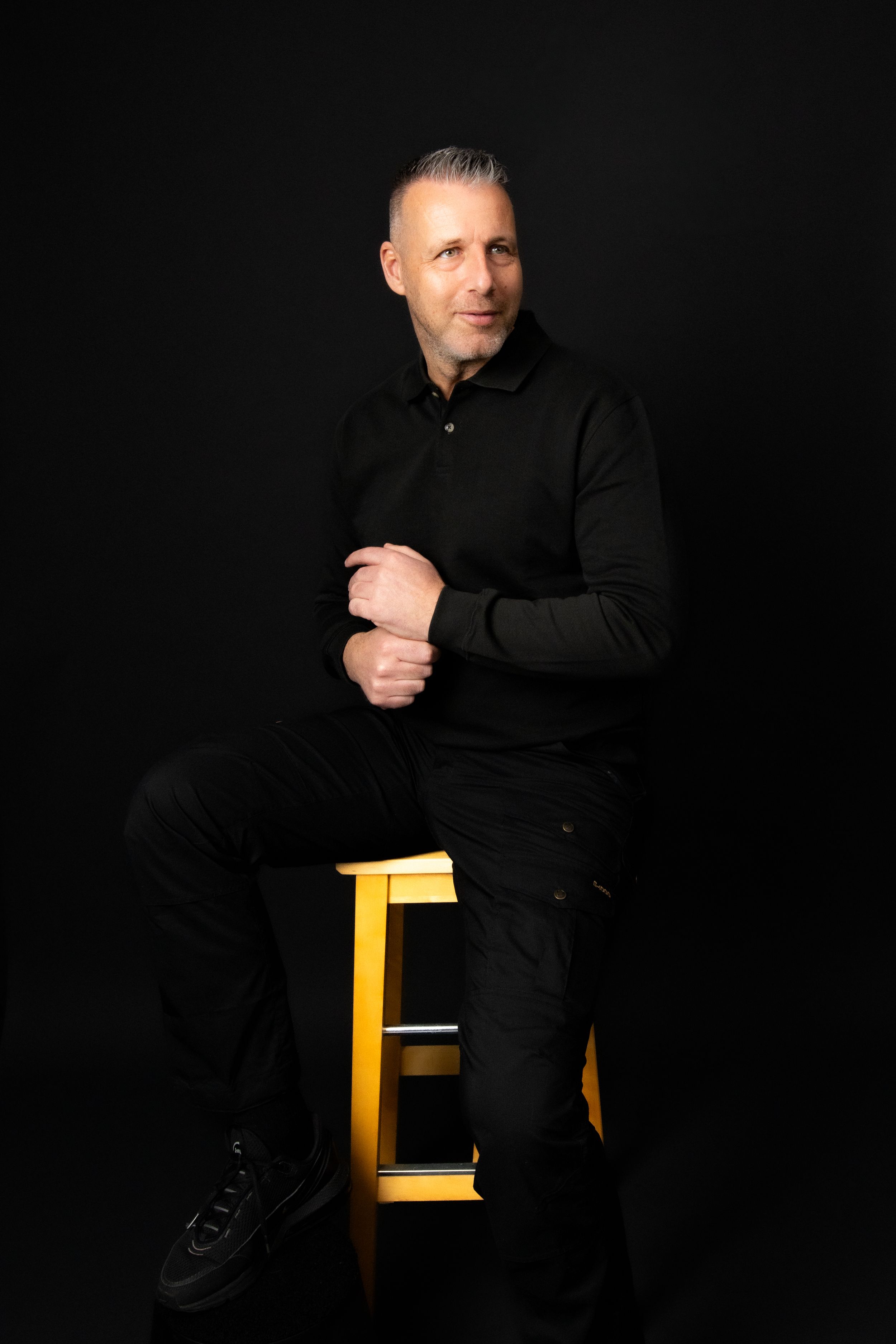 A dramatic black and white portrait series showing a person in black attire posing with a yellow chair against dark background.