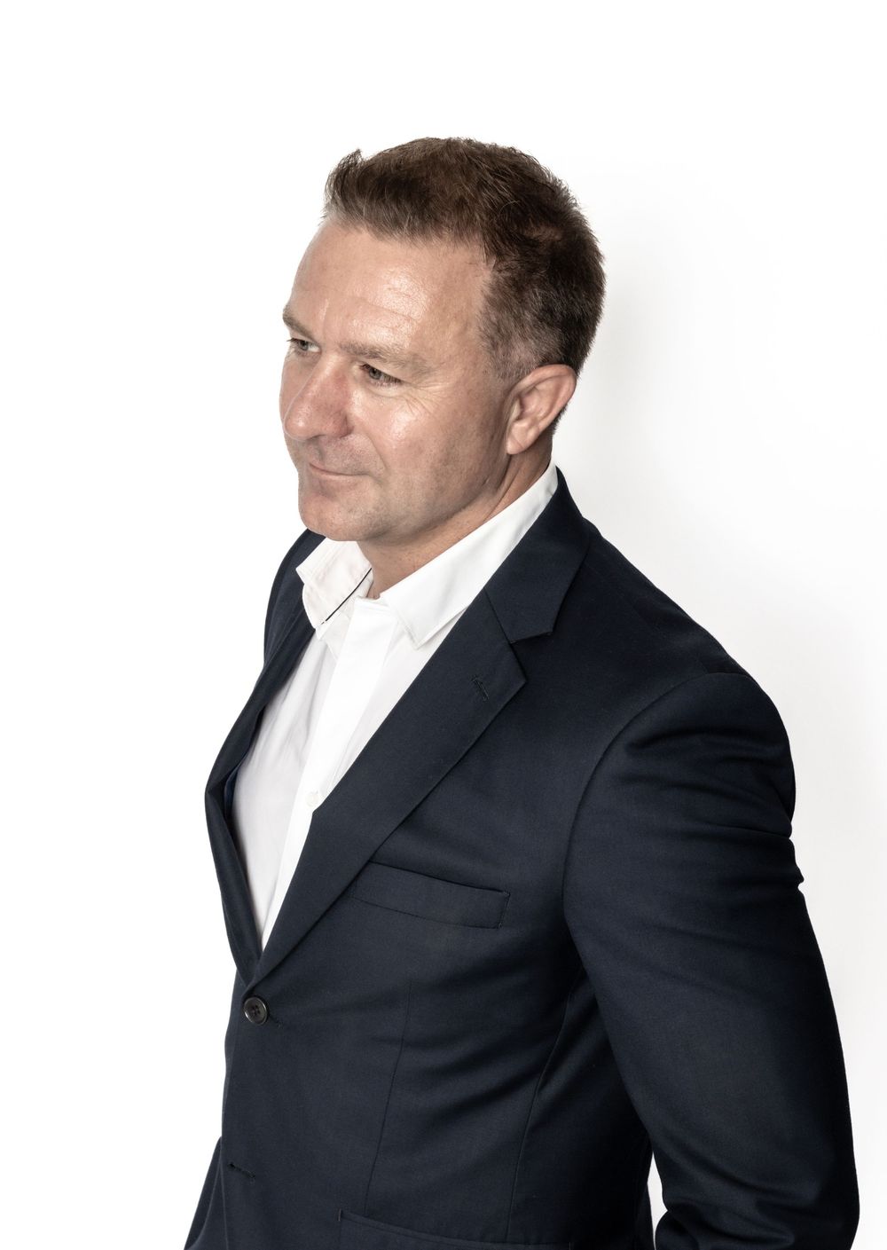 Professional profile photo of a middle-aged individual in a black suit jacket and white dress shirt against white background.