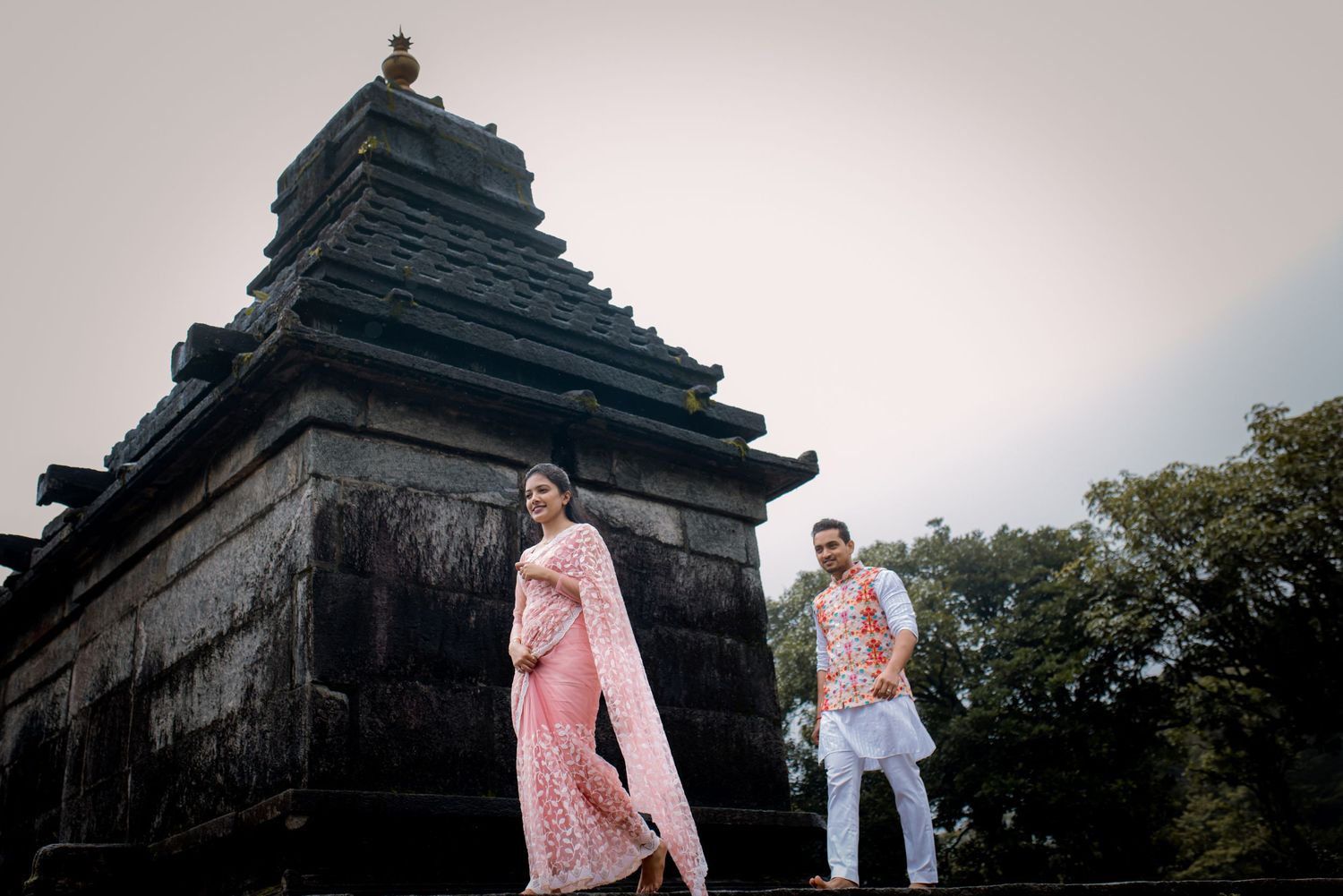 Couple poses near ancient temple structure in traditional Indian attire.