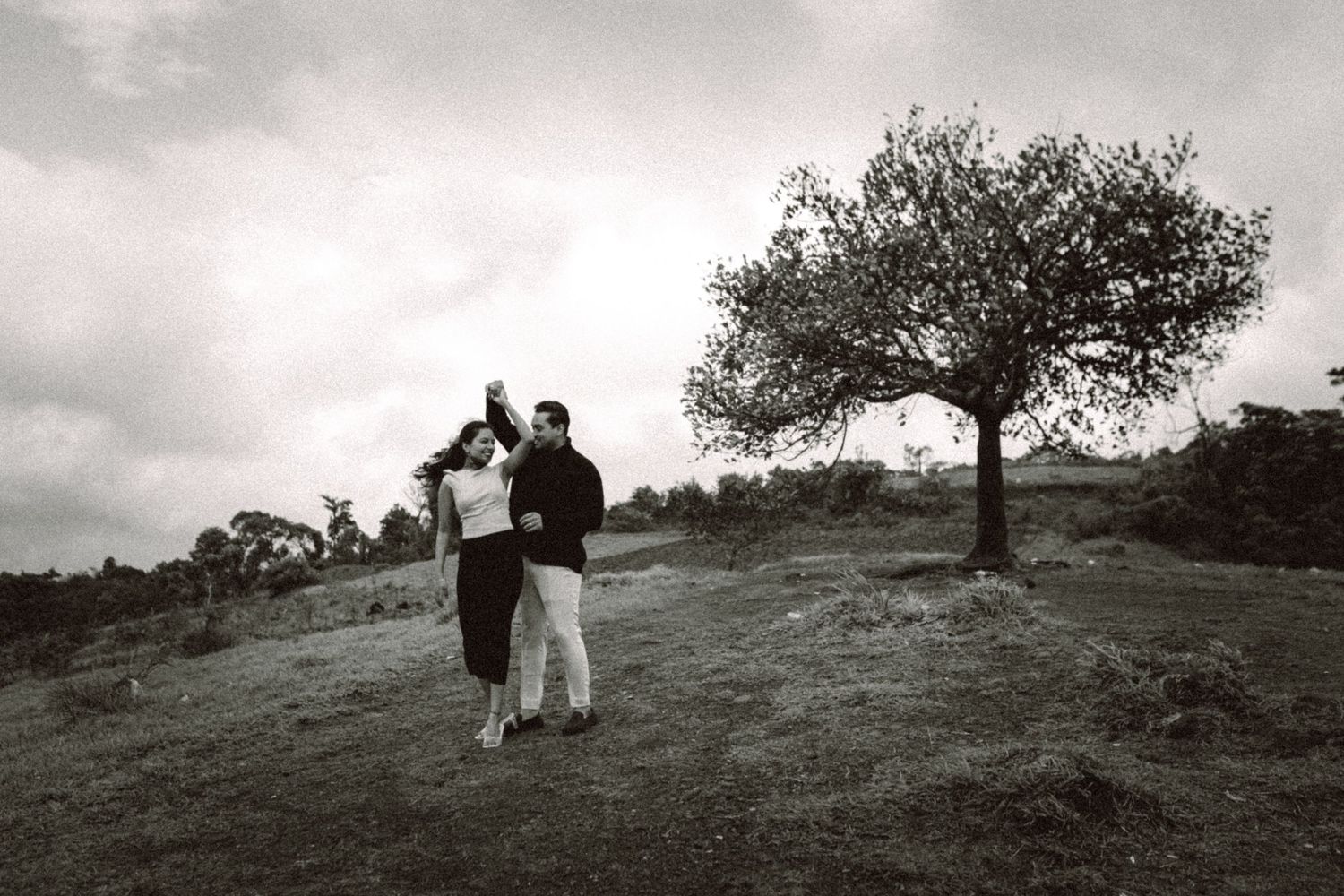 Black and white panoramic shot of two people walking on a grassy hillside.