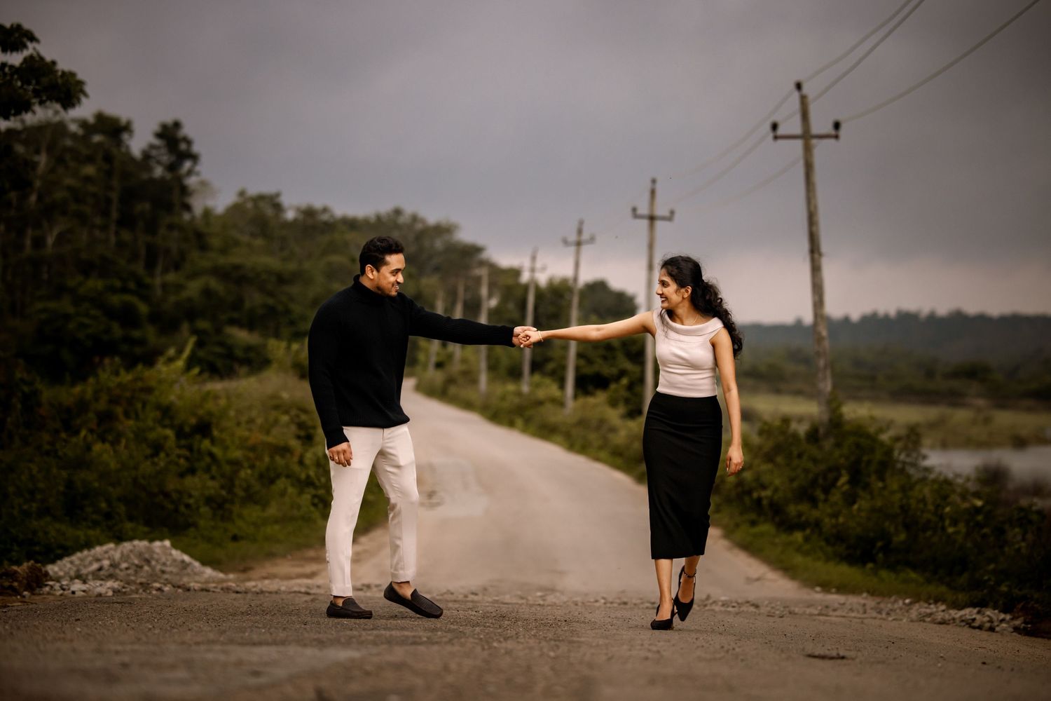 A couple walks along a rural road with utility poles in the background.