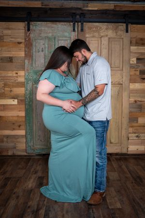 A couple shares an intimate moment against a rustic wooden wall backdrop during a maternity photo session.