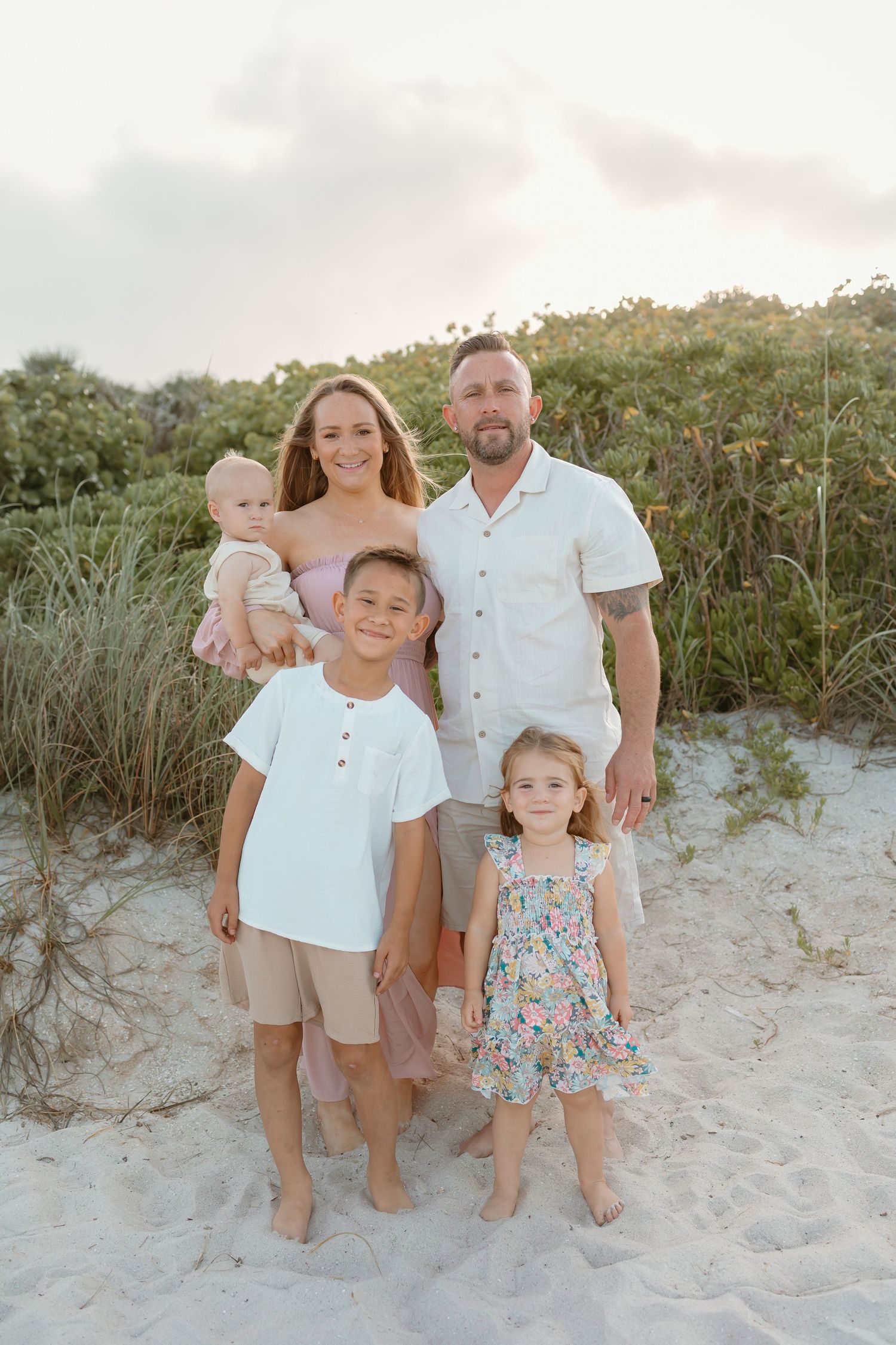 Family portrait session on a sandy beach with dunes and sea grass at sunset.