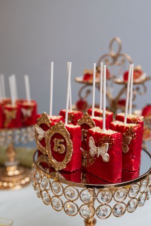 Red cake pops with gold frames, butterfly accents and a number 15 topper displayed on a crystal-trimmed gold dessert stand.