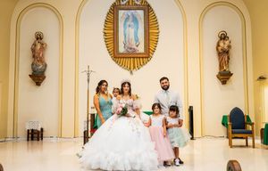 Quinceañera in a white ball gown poses at a church altar with family members and two young girls beneath a Virgin of Guadalupe image.
