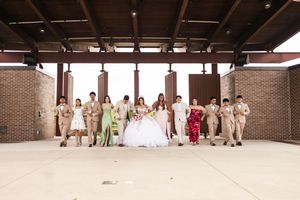Bride in a white gown walks with her wedding party in tan suits and green and red dresses under a brick pavilion.