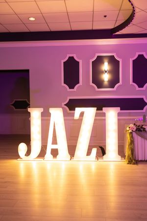 Illuminated marquee letters spell JAZI on the wood dance floor of a purple-lit banquet hall with a decorated table.