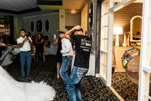 Guests dance and celebrate on the floor of a reception hall at a quinceañera while the honoree's white gown trails at the left.