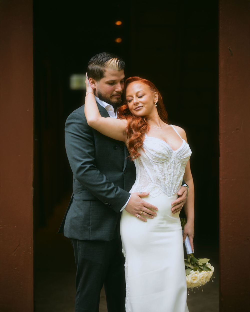 A romantic wedding couple embraces in an intimate moment against a dark backdrop.