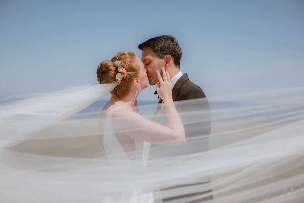 A romantic wedding couple embraces under flowing white veil during their outdoor photo session.