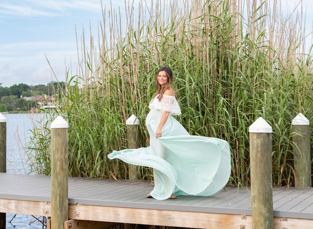 Maternity photography portraits in Bayview Park Pensacola, FL, woman twirls green skirt on dock