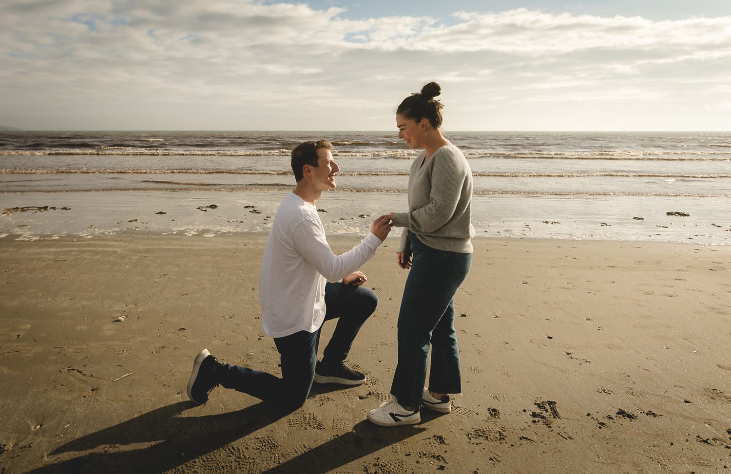 Couple sharing intimate moment at beach with overcast sky and sand in foreground.