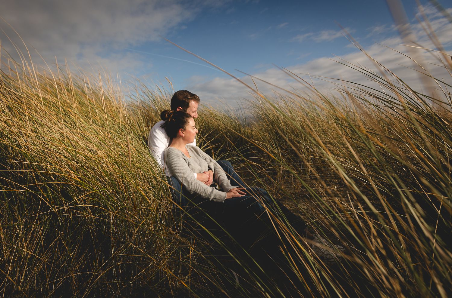 Partners resting in windswept coastal grass with moody sky overhead.