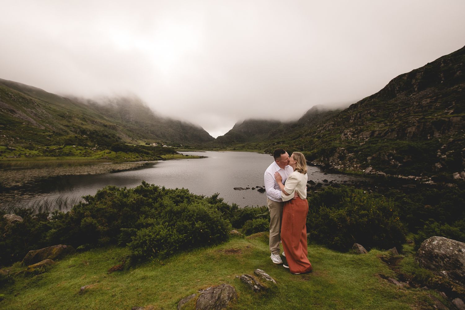 Misty mountains and seaside cliffs line a winding coastal road in dramatic Irish landscape during overcast weather.