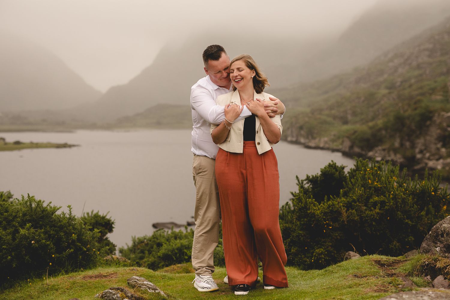 Couple shares romantic moment on cliffside overlooking misty mountain lake.
