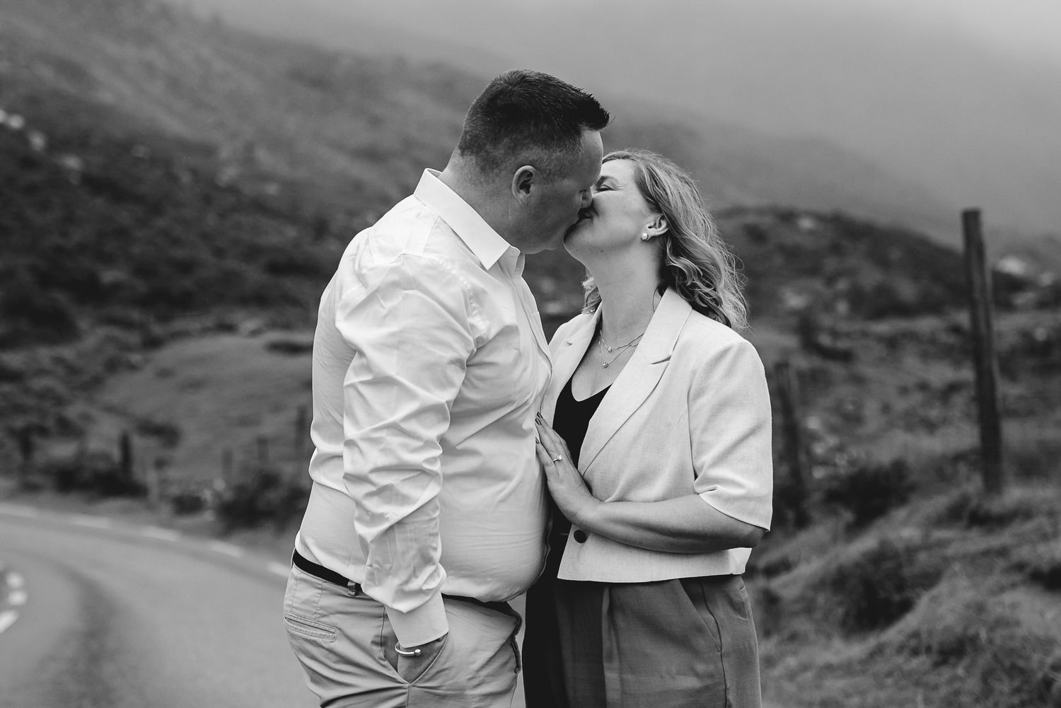 A romantic couple shares intimate moments in a scenic mountainous landscape during a black and white photoshoot.