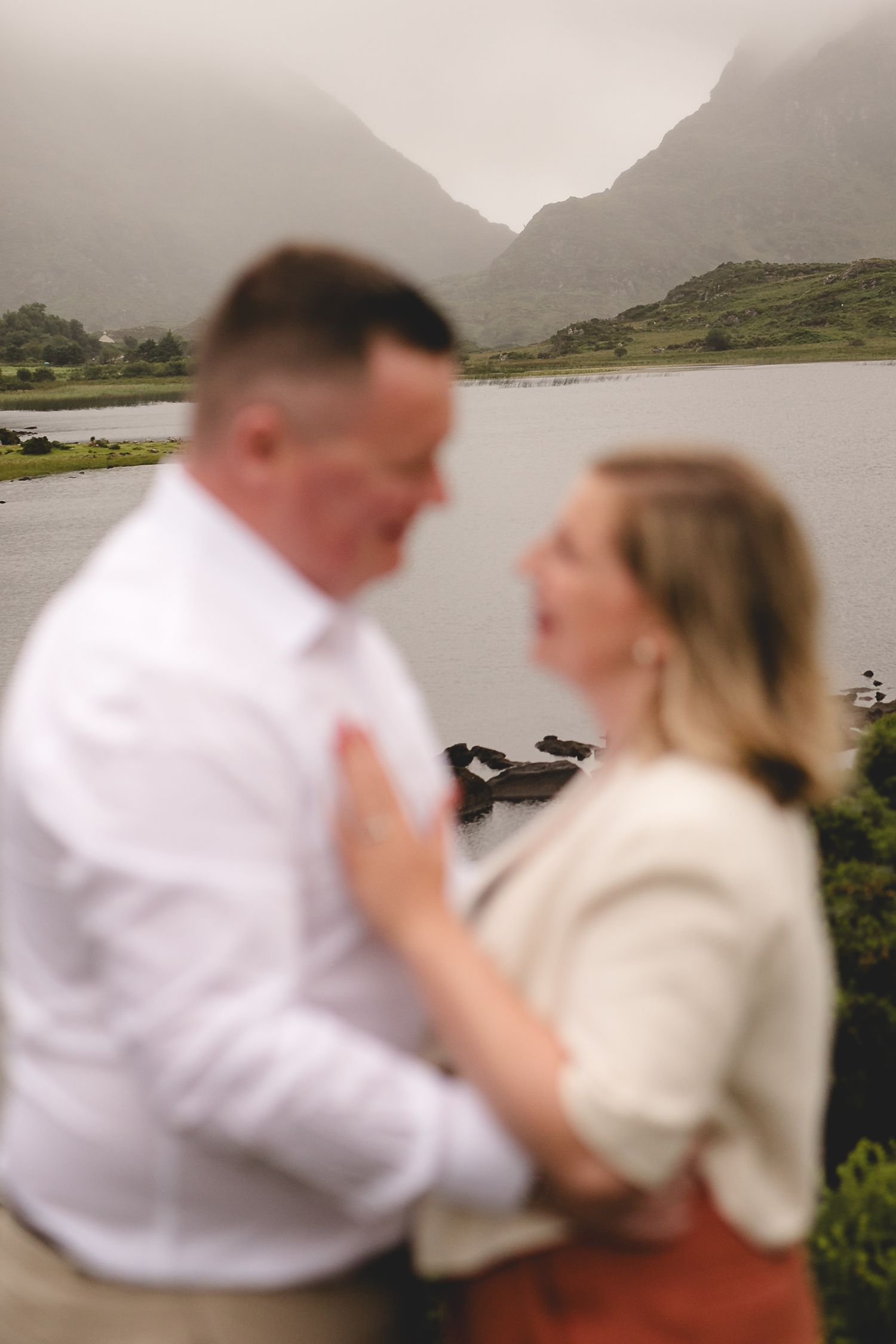 Two people walking along a mountain road overlooking a scenic lake on a misty day.
