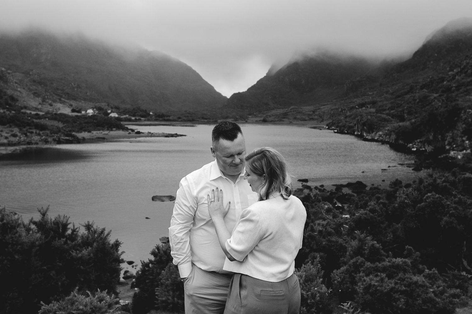 Two people share a tender embrace with mountains and lake views in the background.