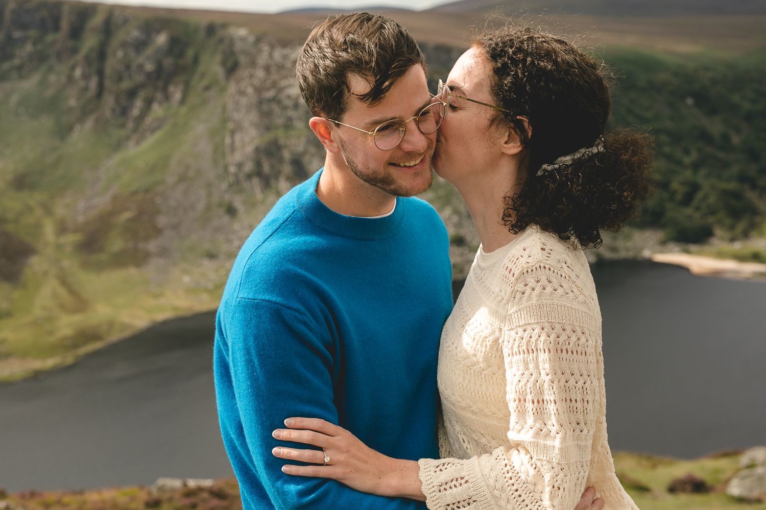 A couple sharing an intimate moment on a hilltop overlooking a lake in scenic mountain landscape.