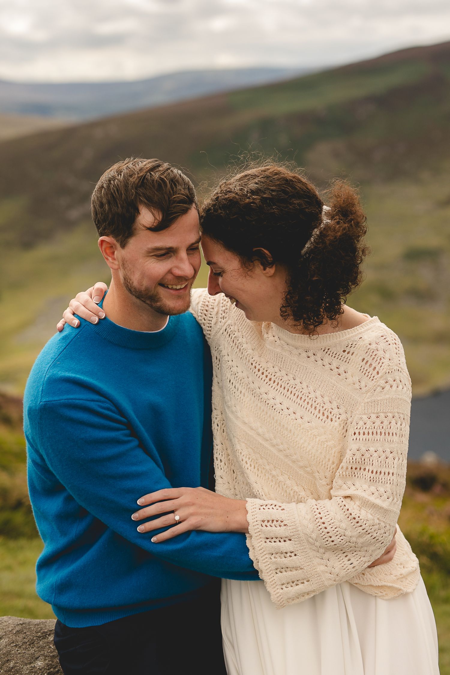 A romantic moment between a couple embracing on a hillside, with the man in blue and woman in white lace.
