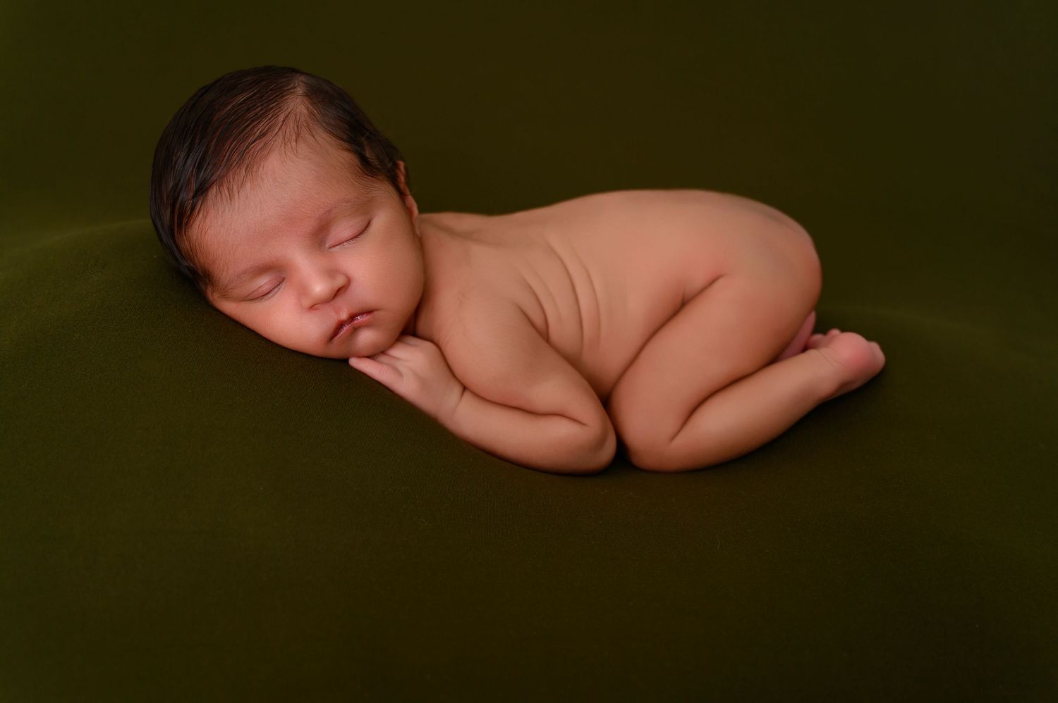 Minimalist newborn photography with baby sleeping against dark background.