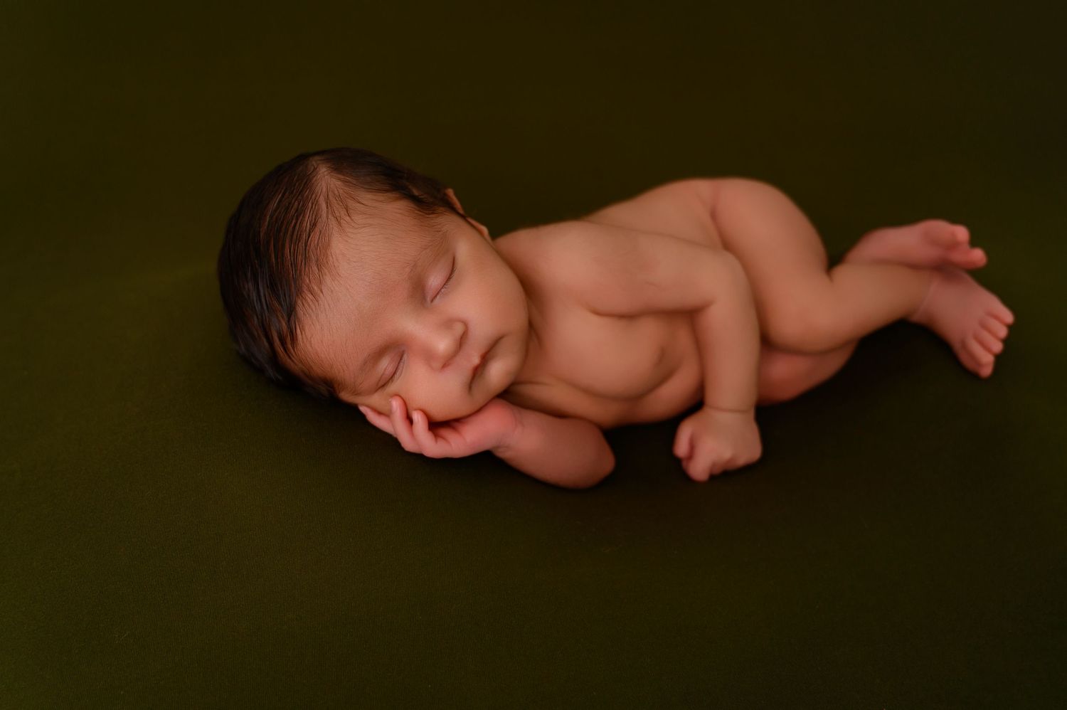 Simple studio portrait of sleeping newborn on dark backdrop with dramatic lighting.