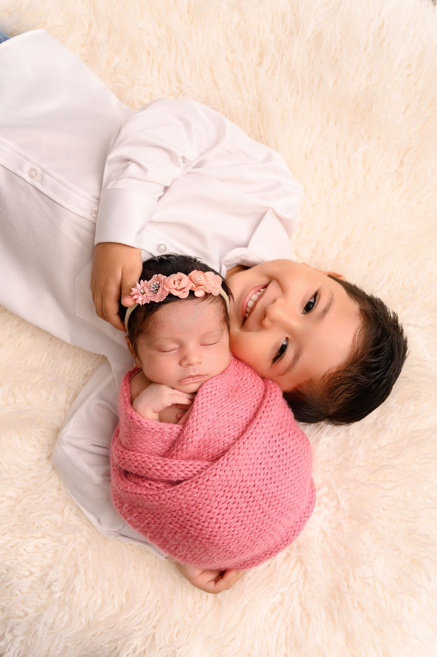 Newborn baby wrapped in pink knit blanket lying on cream colored fur rug in artistic photography series.