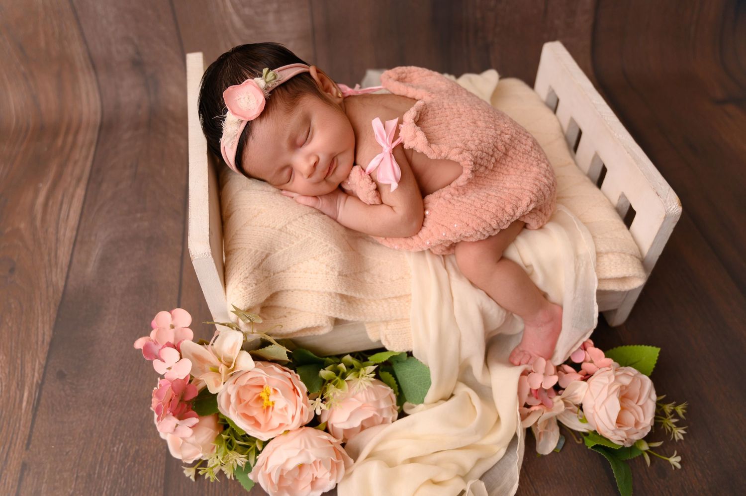 Newborn photography setup with pink roses and white textured blankets on wooden surface.