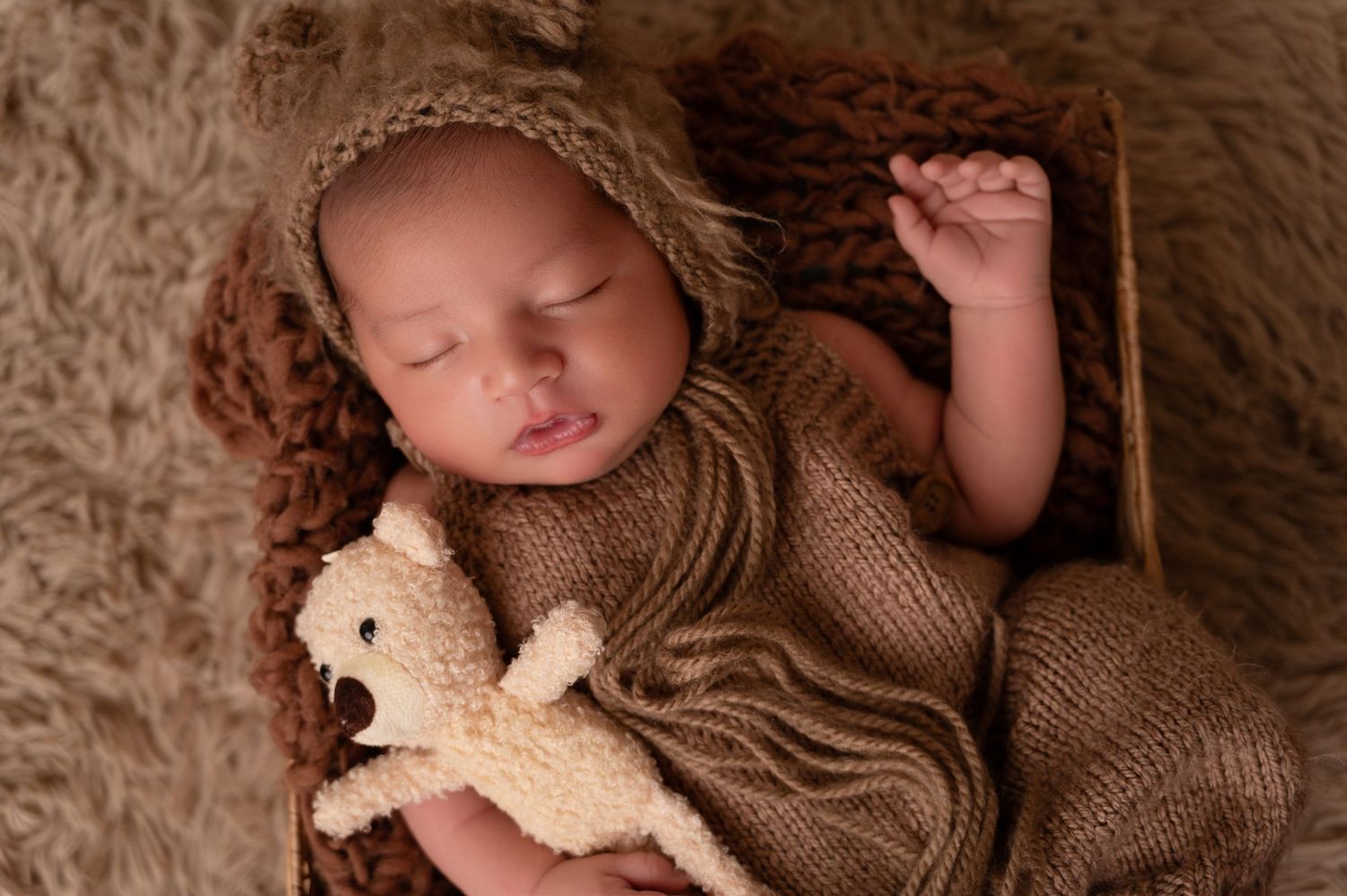 Baby wearing brown knit bear outfit sleeping on textured fur backdrop.