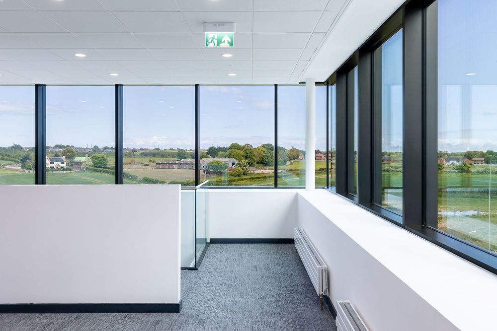 Bright modern interior corridor with large floor-to-ceiling windows overlooking a green landscaped view.