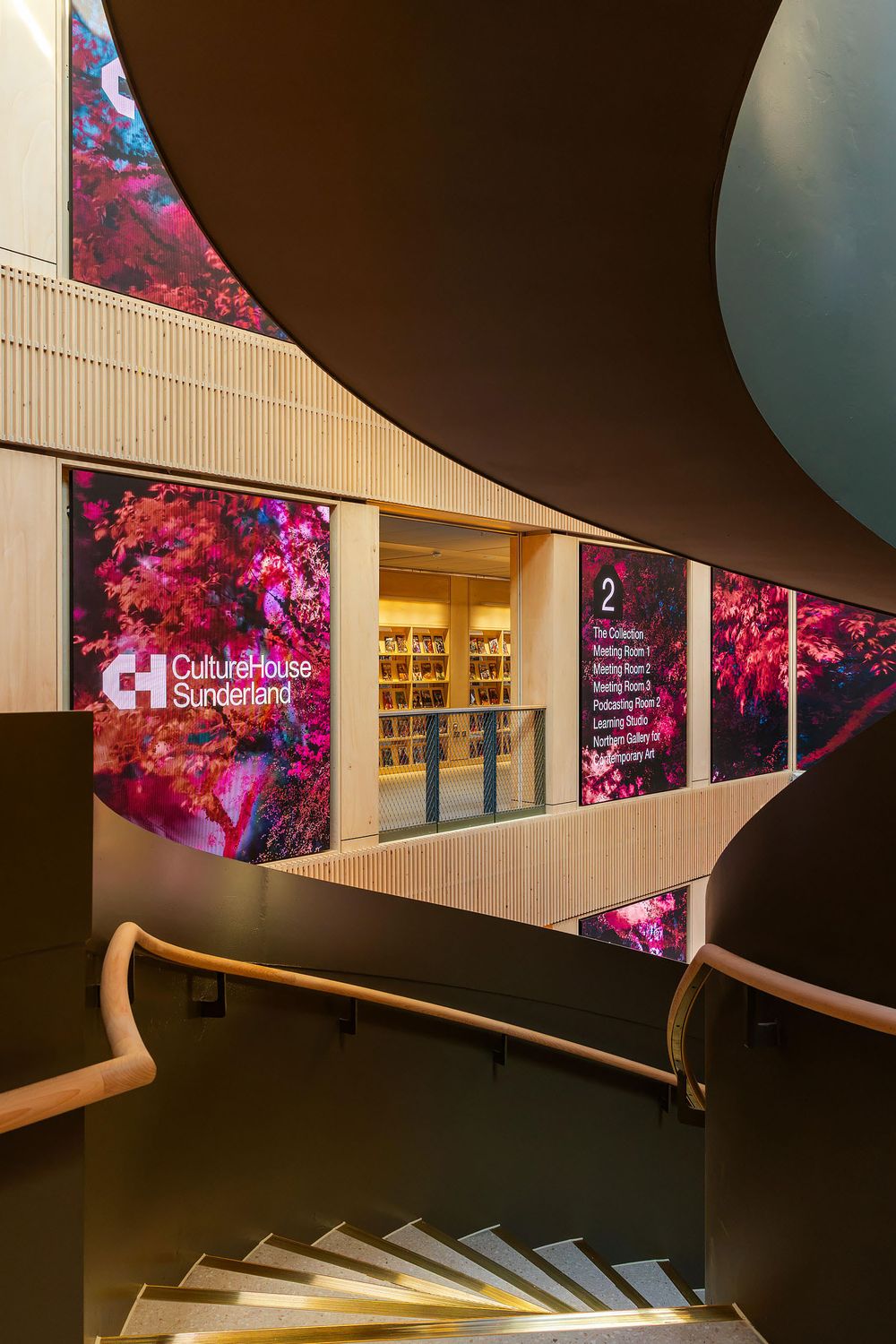 Contemporary curved staircase with illuminated steps and vibrant digital artwork displays in a modern cultural centre interior.
