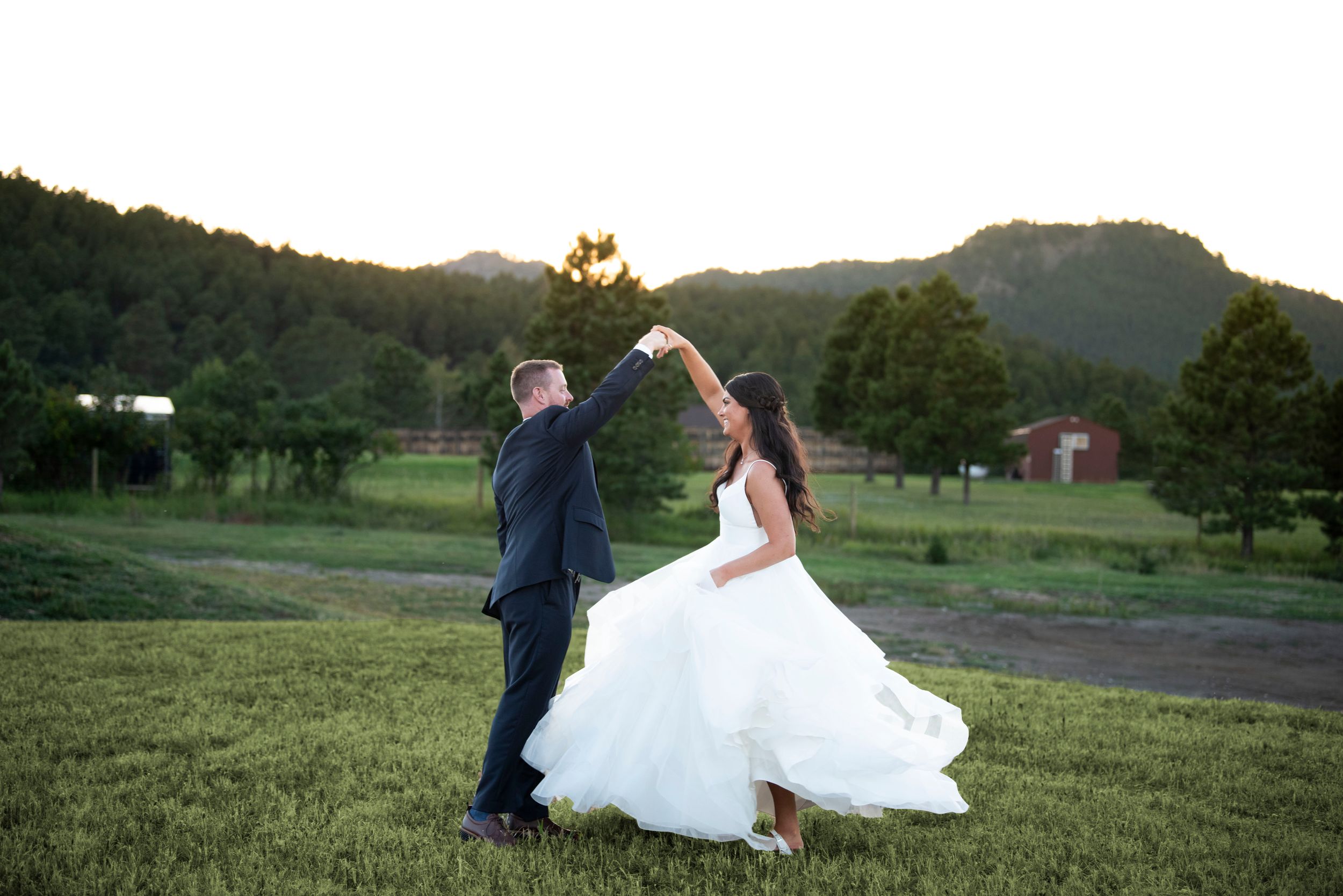Newlywed couple dancing in a grassy field at sunset.