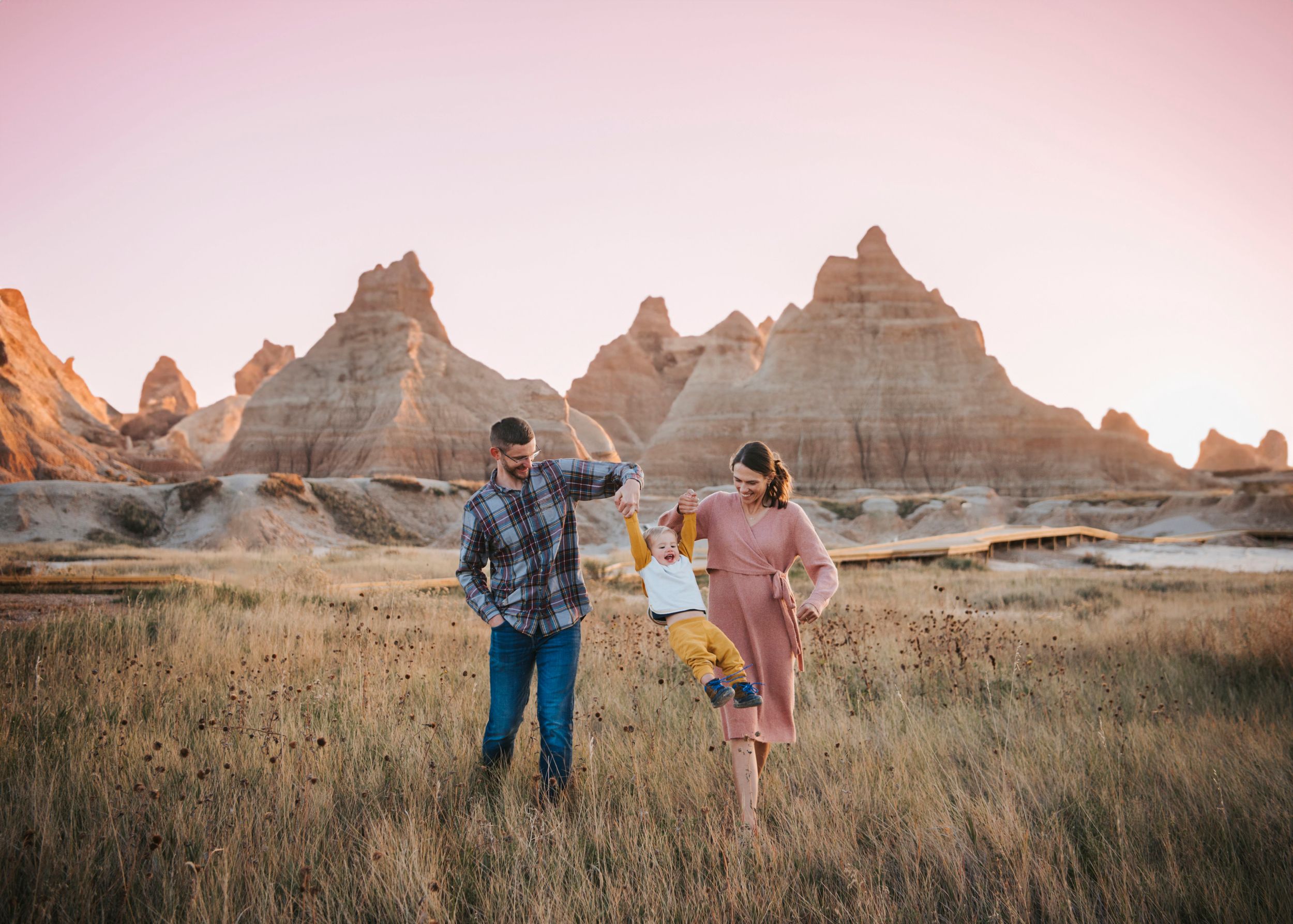 Couple walking through prairie grass with rock formations in background at sunset in the Badlands.