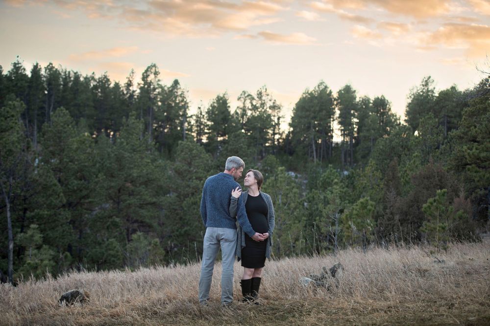 A couple takes an evening stroll through a golden meadow with pine trees.