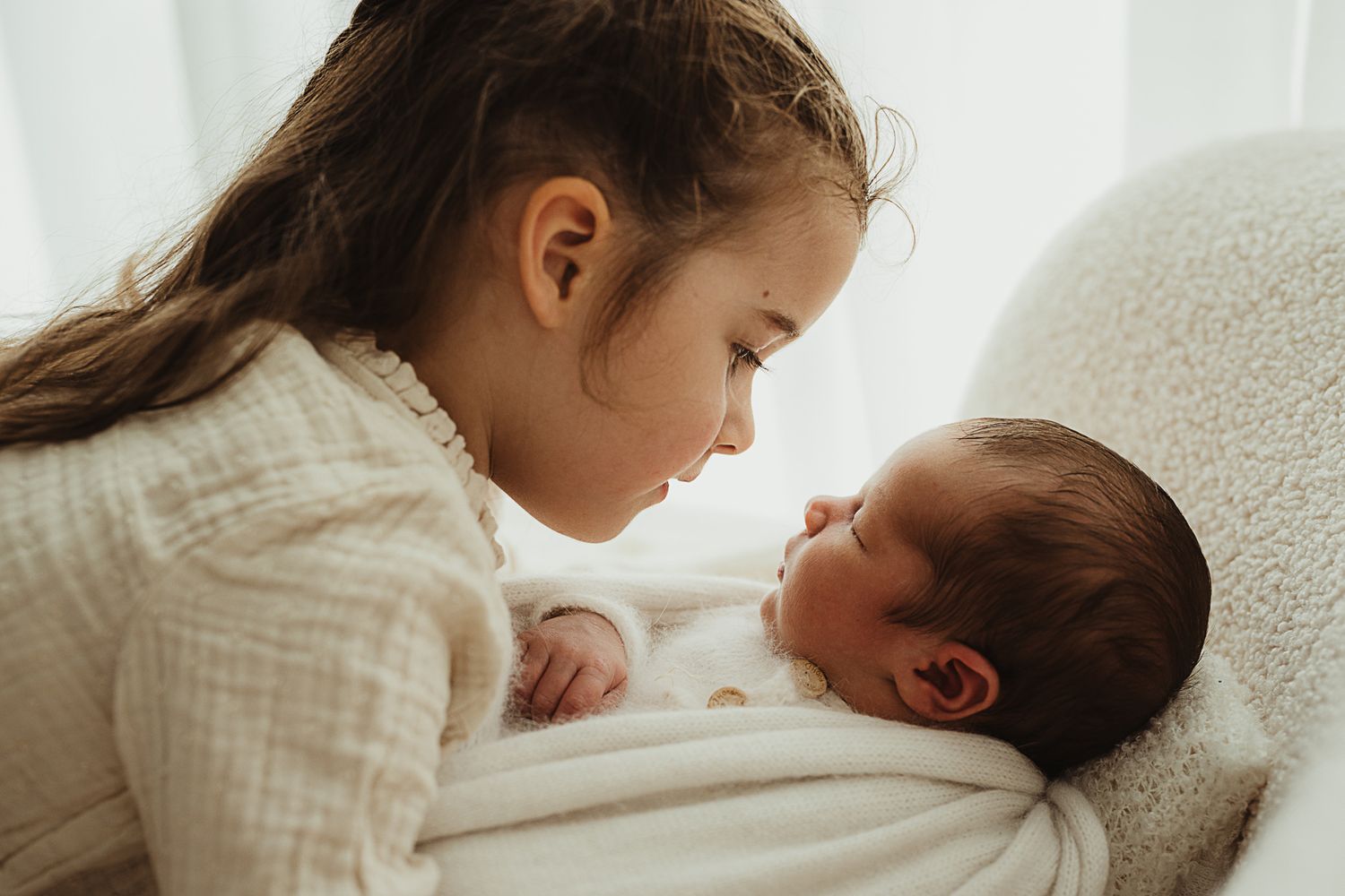 A sleeping newborn baby is wrapped in soft white blankets in gentle lighting.