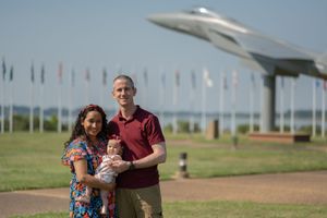Casual outdoor portraits at military memorial site with vintage aircraft and flag display.