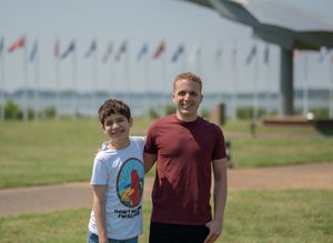Family photography session near military aircraft display with colorful flags waving in background.