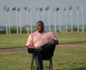 Someone sitting in a chair on a grassy field with rows of international flags waving in the background.