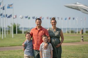 A group poses together on a sunny day with international flags and an aircraft display visible in the background.