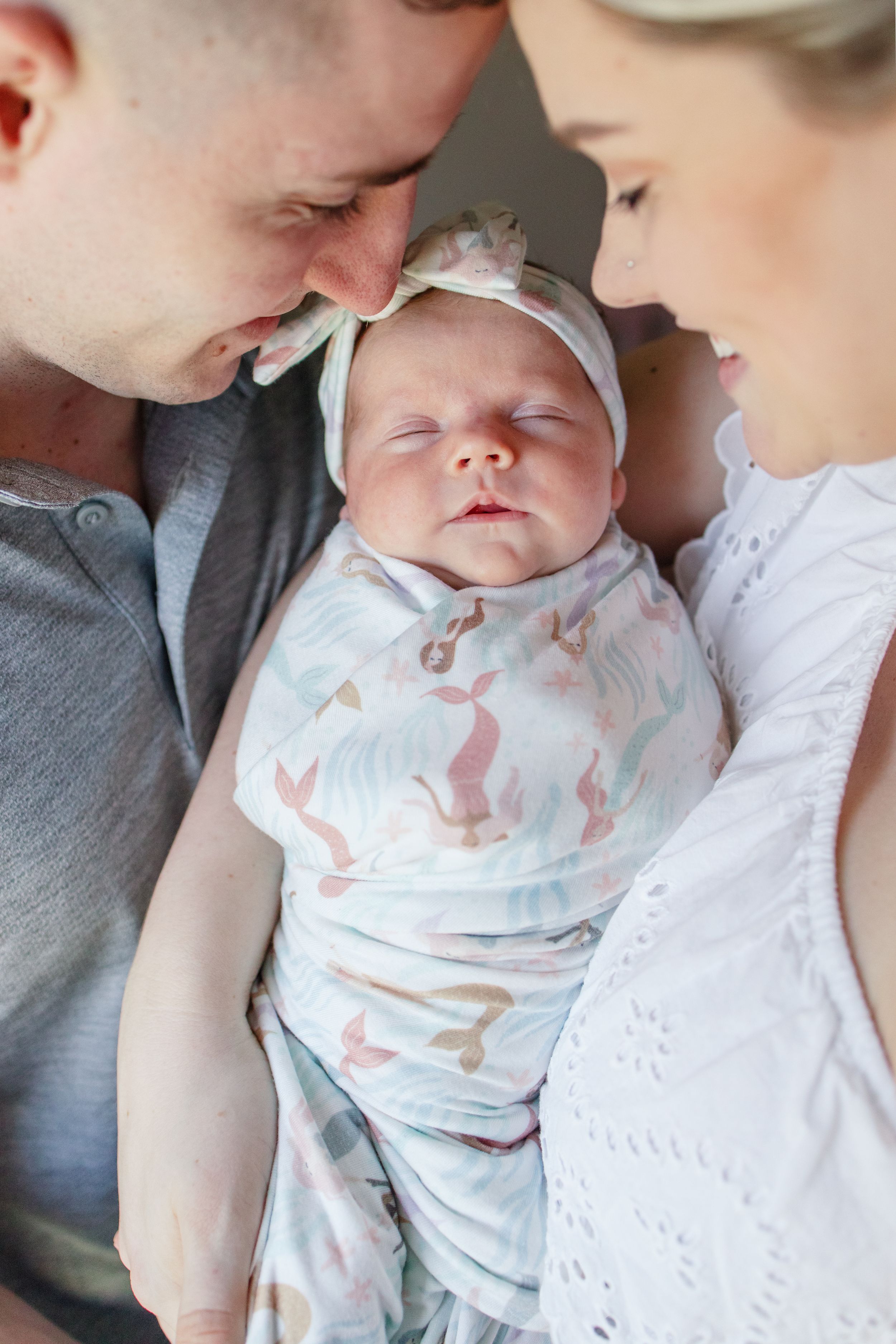 A series of tender moments between parents and their sleeping newborn baby swaddled in a white patterned blanket.