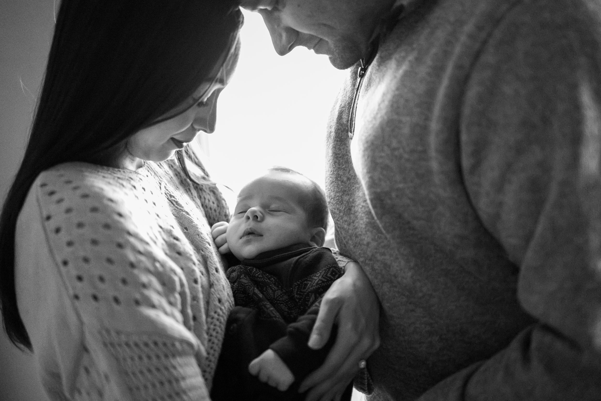 Black and white intimate family portrait of parents gazing lovingly at their newborn baby.