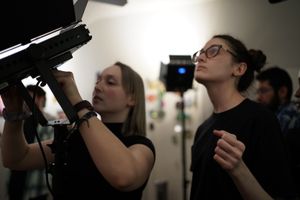 Film crew members operate professional cameras in dimly lit studio setting.