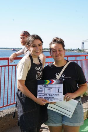 Production crew members posing with a film slate against waterfront backdrop.