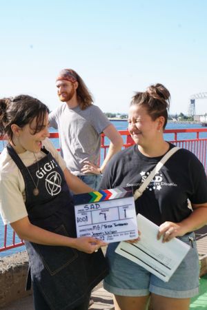 Film crew members on location holding a movie slate near a waterfront.