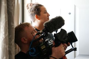 Two camera operators filming with professional equipment by a window.