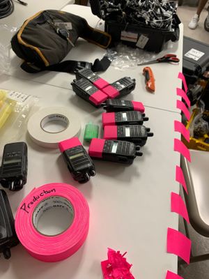 Production equipment including pink gaffer tape and black electronic devices laid out on a table.