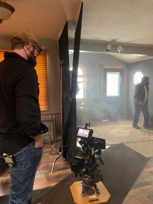 Film crew member operating camera equipment in a smoke-filled room with natural lighting.