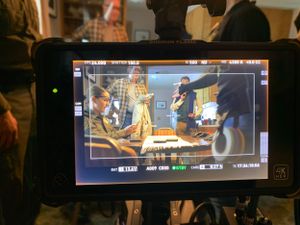 Camera monitor display showing actors in a dramatic indoor scene.