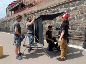 Film crew members setting up camera equipment against a stone wall exterior.