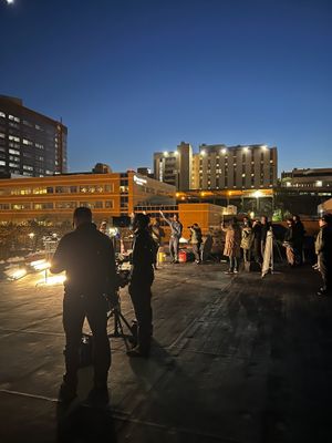 Film crew shooting a night scene on a rooftop with city buildings in the background.